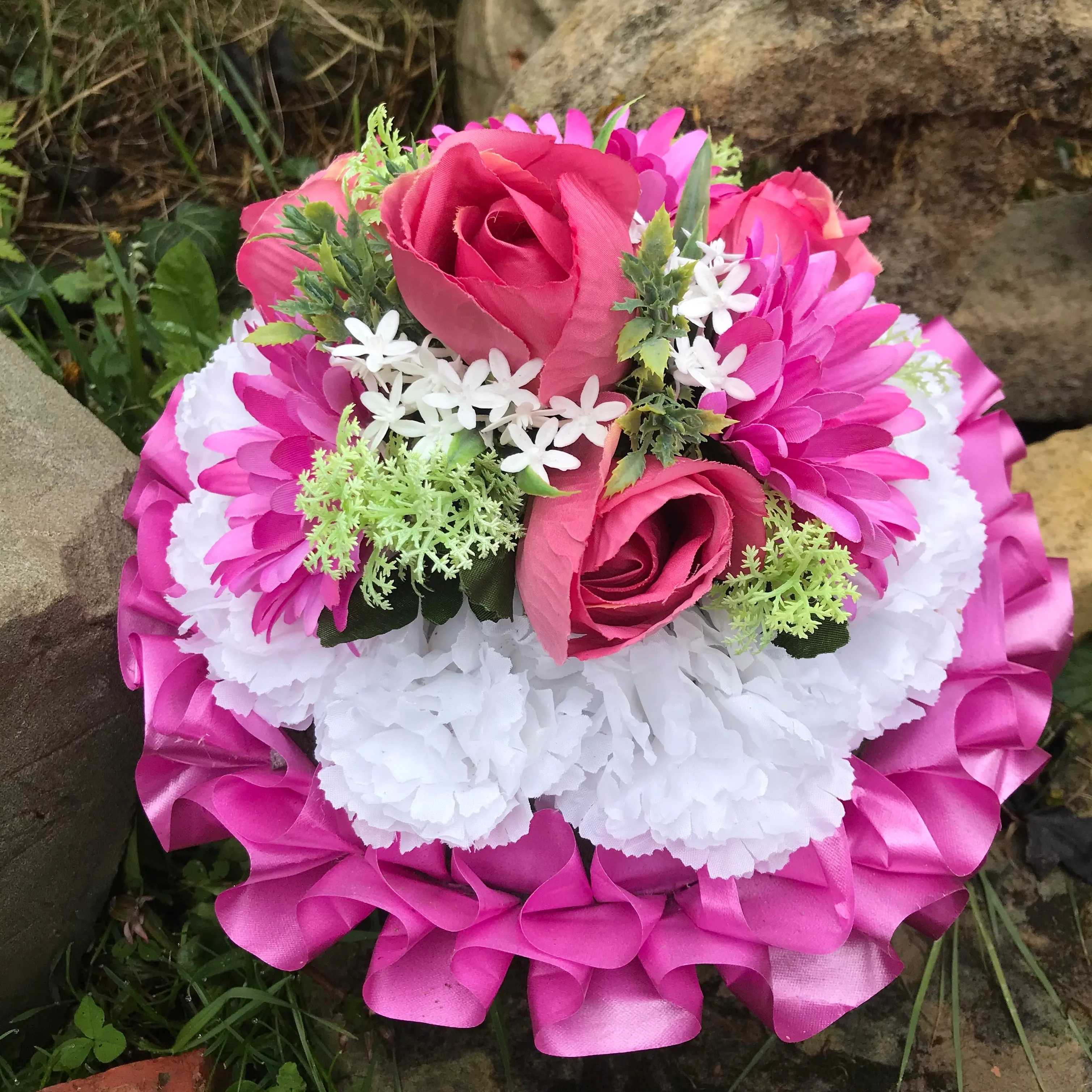 A graveside funeral posy of artificial silk flowers in shades of pink & white